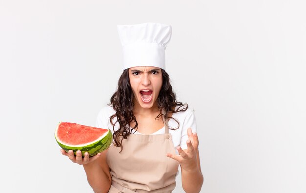 Hispanic pretty chef woman looking angry, annoyed and frustrated and holding a watermelon