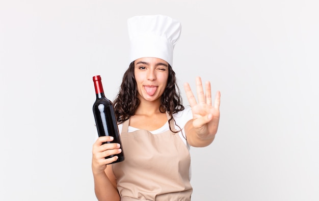 Bella donna ispanica chef sorridente e dall'aspetto amichevole, che mostra il numero quattro e tiene in mano una bottiglia di vino