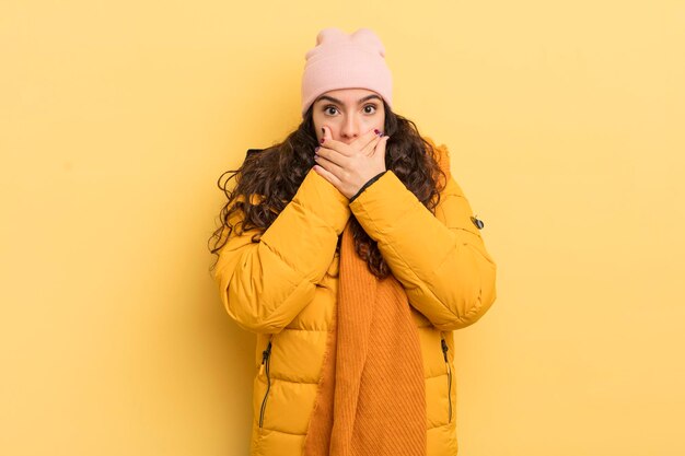 Hispanic pretty woman covering mouth with hands with a shocked, surprised expression, keeping a secret or saying oops