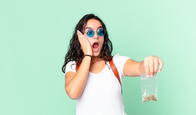 Hispanic pretty woman feeling happy, excited and surprised and holding a marihuana bag