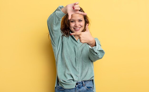 Hispanic pretty woman feeling happy, friendly and positive, smiling and making a portrait or photo frame with hands