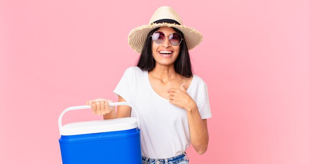 Hispanic pretty woman feeling happy and pointing to self with an excited with a picnic portable refrigerator