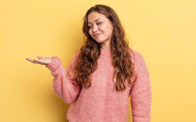 Hispanic pretty woman feeling happy and smiling casually, looking to an object or concept held on the hand on the side