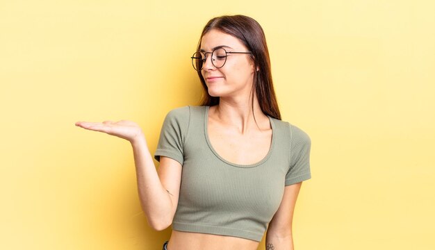 Hispanic pretty woman feeling happy and smiling casually, looking to an object or concept held on the hand on the side