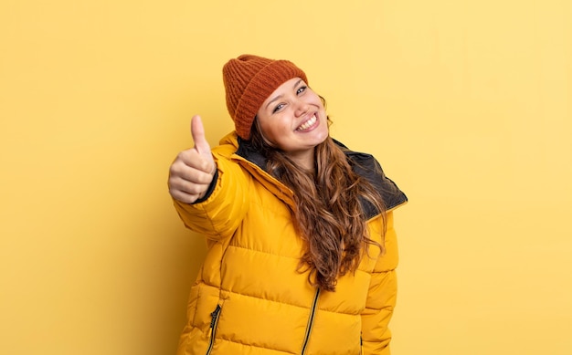 Hispanic pretty woman feeling proud,smiling positively with thumbs up. winter clothes