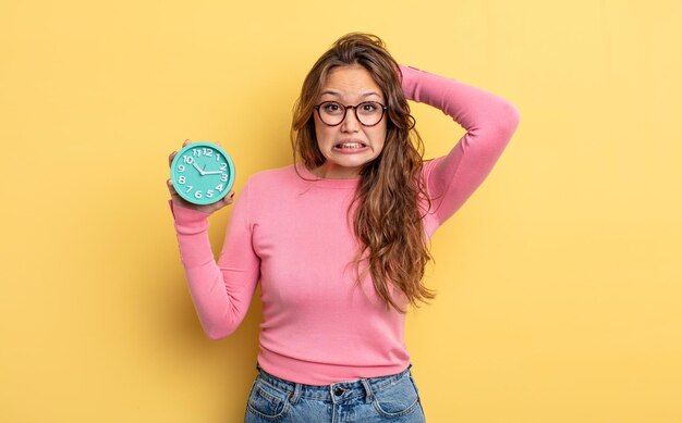 Hispanic pretty woman feeling stressed, anxious or scared, with hands on head. alarm clock concept