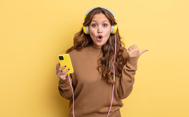 Hispanic pretty woman looking astonished in disbelief. headphones and smartphone concept