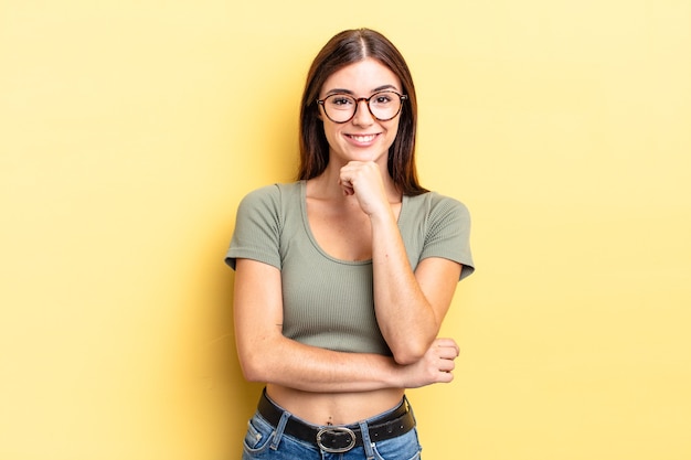 Hispanic pretty woman looking happy and smiling with hand on chin, wondering or asking a question, comparing options