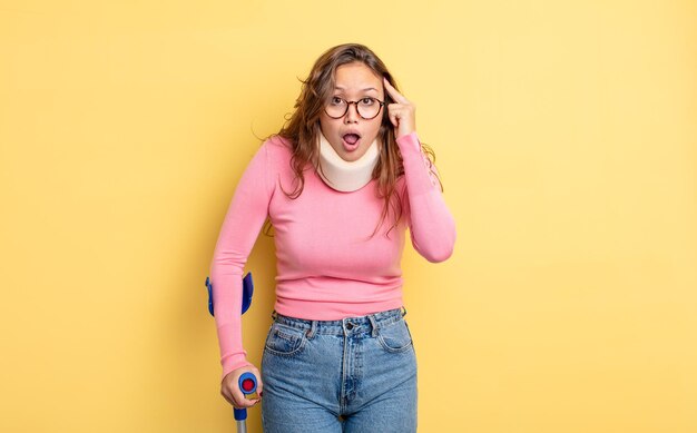 Hispanic pretty woman looking surprised, realizing a new thought, idea or concept. crutch and collar accident