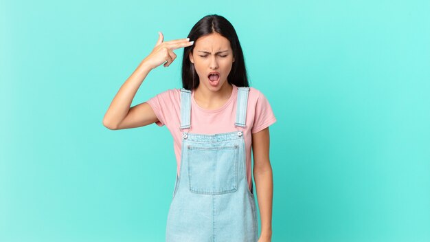 Hispanic pretty woman looking unhappy and stressed, suicide gesture making gun sign