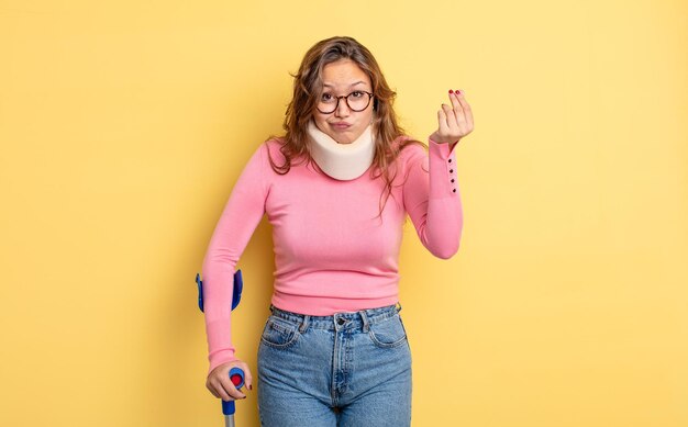 Hispanic pretty woman making capice or money gesture, telling you to pay. crutch and collar accident