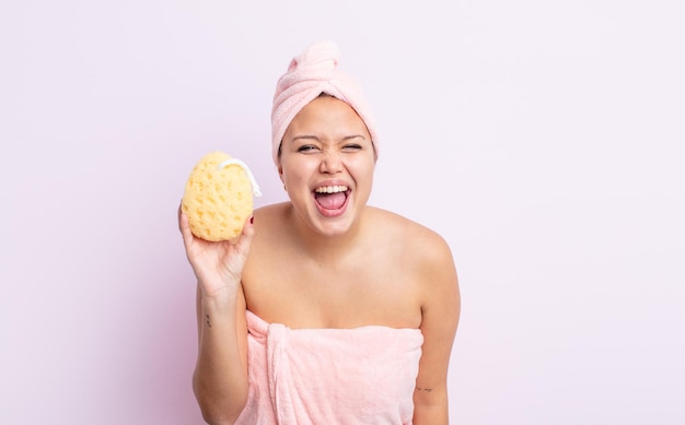 Hispanic pretty woman shouting aggressively, looking very angry. bathrobe and sponge concept