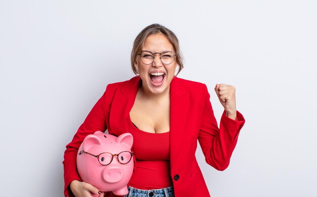 Hispanic pretty woman shouting aggressively with an angry expression. piggy bank concept