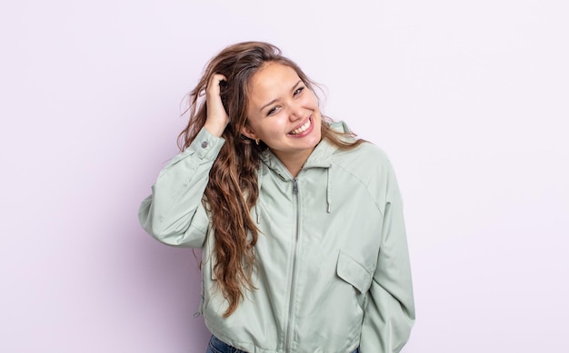 Hispanic pretty woman smiling cheerfully and casually, taking hand to head with a positive, happy and confident look