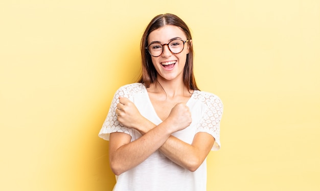 Hispanic pretty woman smiling cheerfully and celebrating, with fists clenched and arms crossed, feeling happy and positive