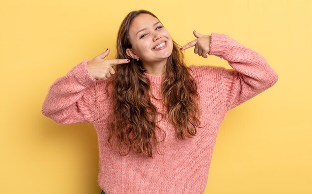 Hispanic pretty woman smiling confidently pointing to own broad smile positive relaxed satisfied attitude