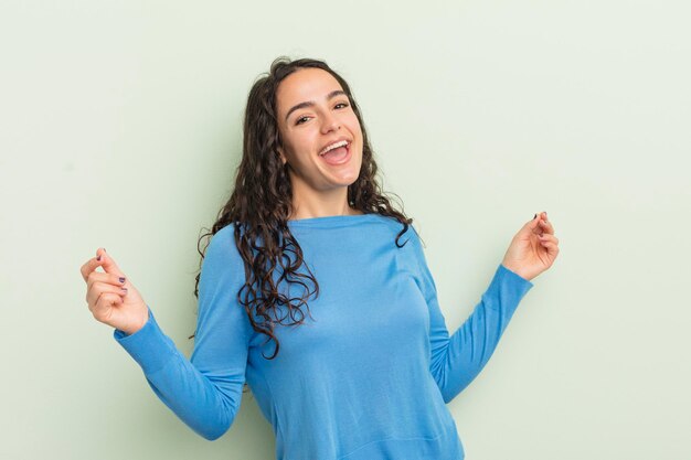 Hispanic pretty woman smiling, feeling carefree, relaxed and happy, dancing and listening to music, having fun at a party