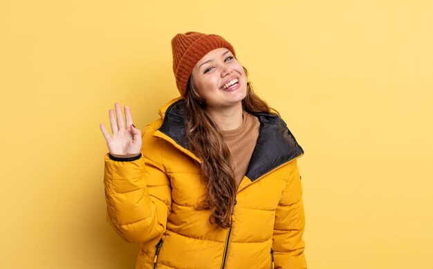 Hispanic pretty woman smiling happily, waving hand, welcoming and greeting you. winter clothes