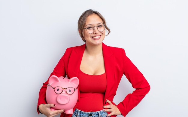 Hispanic pretty woman smiling happily with a hand on hip and confident. piggy bank concept