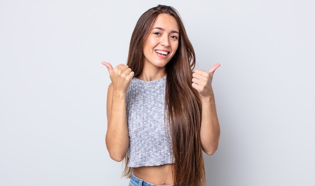 hispanic pretty woman smiling joyfully and looking happy, feeling carefree and positive with both thumbs up