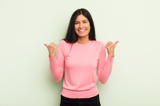 Hispanic pretty woman smiling joyfully and looking happy feeling carefree and positive with both thumbs up