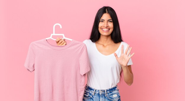 Hispanic pretty woman smiling and looking friendly, showing number five and holding a choosen cloth