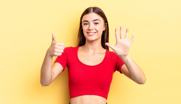 Hispanic pretty woman smiling and looking friendly, showing number six or sixth with hand forward, counting down