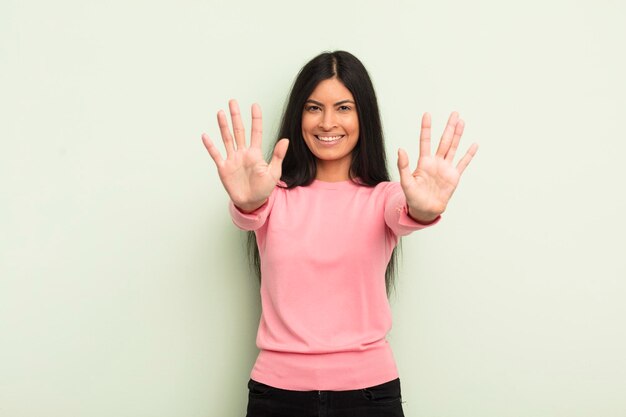 Hispanic pretty woman smiling and looking friendly showing number ten or tenth with hand forward counting down