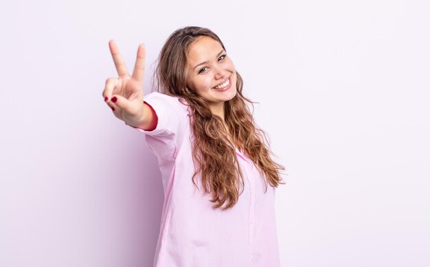 Hispanic pretty woman smiling and looking happy, carefree and positive, gesturing victory or peace with one hand