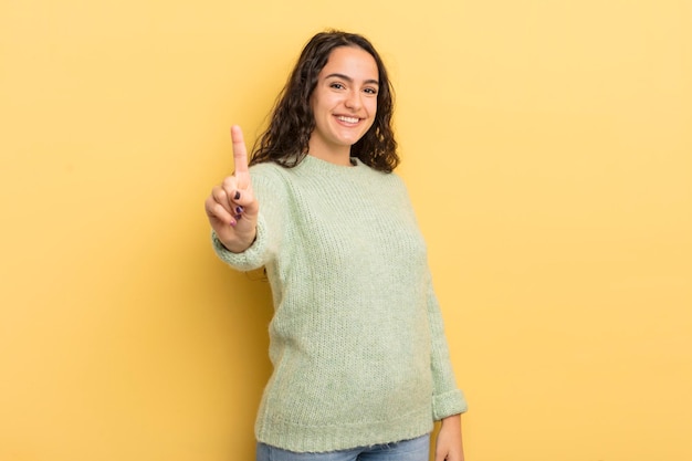 Hispanic pretty woman smiling proudly and confidently making number one pose triumphantly feeling like a leader