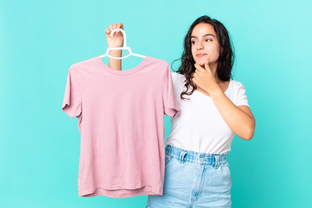 hispanic pretty woman smiling with a happy, confident expression with hand on chin choosing a cloth