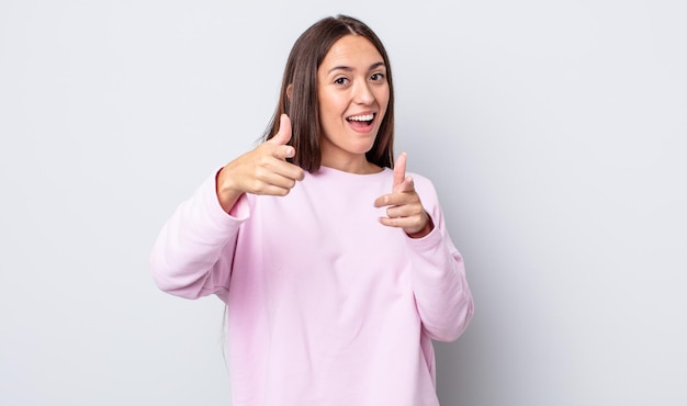 Foto donna graziosa ispanica che sorride con un atteggiamento felice positivo positivo che indica la macchina fotografica che fa il segno della pistola con le mani