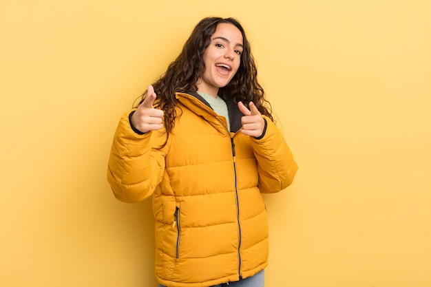 Photo hispanic pretty woman smiling with a positive successful happy attitude pointing to the camera making gun sign with hands