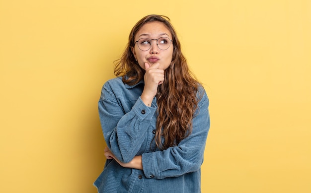 Hispanic pretty woman thinking, feeling doubtful and confused, with different options, wondering which decision to make