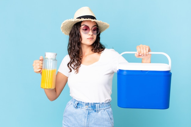 Hispanic pretty woman with a portable fridge and an orange juice