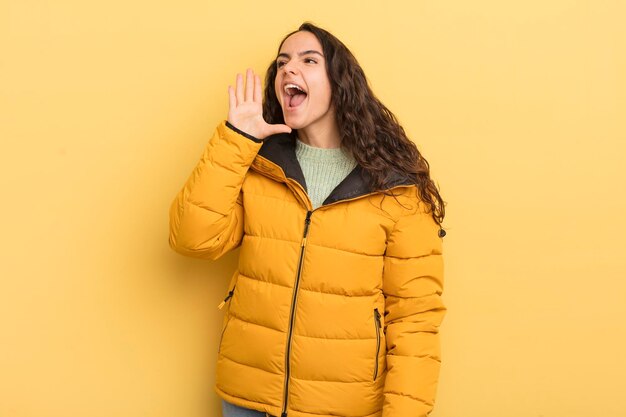 hispanic pretty woman yelling loudly and angrily to copy space on the side, with hand next to mouth