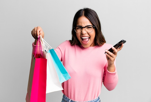 Hispanic pretty young adult woman with shopping bags and her smartphone buy concept