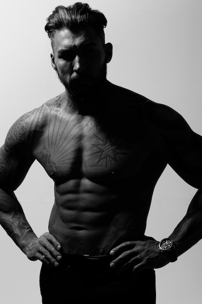 Hispanic shirtless male model with muscular tattooed torso standing with hands in pockets