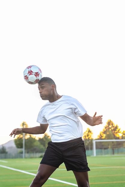 Hispanic soccer player wearing white shirt in field heading foot ball in field