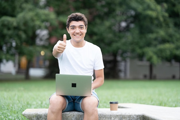 Hispanic student boy with thumbs up in a park