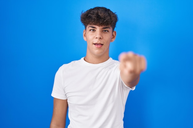 Hispanic teenager standing over blue background pointing displeased and frustrated to the camera angry and furious with you