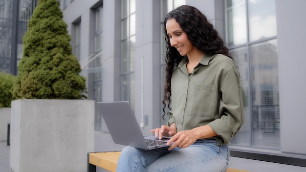 Hispanic woman business lady s businesswoman freelancer sitting on bunch outdoors with laptop