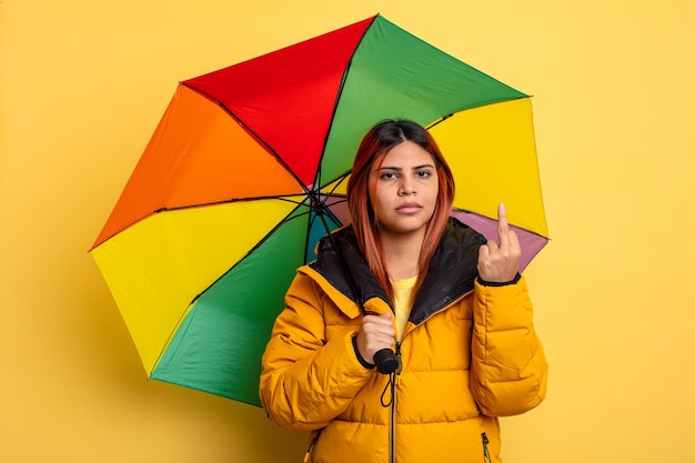 Hispanic woman feeling angry annoyed rebellious and aggressive\
rain and umbrella concept