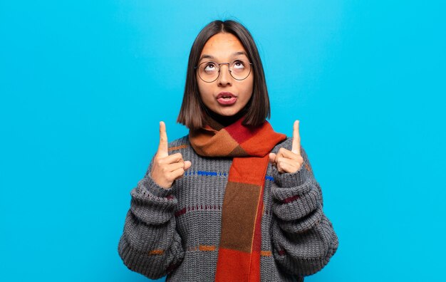 Hispanic woman feeling awed and open mouthed pointing upwards with a shocked and surprised look