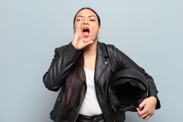 Hispanic woman feeling happy, excited and positive, giving a big shout out with hands next to mouth, calling out