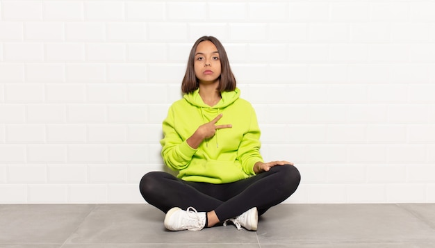 Hispanic woman feeling happy, positive and successful, with hand making v shape over chest, showing victory or peace