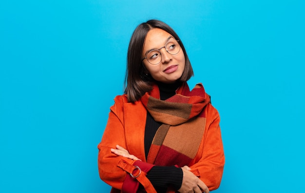 Hispanic woman feeling happy, proud and hopeful, wondering or thinking, looking up to copy space with crossed arms