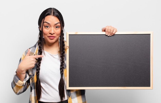 Hispanic woman feeling happy, surprised and proud, pointing to self with an excited, amazed look