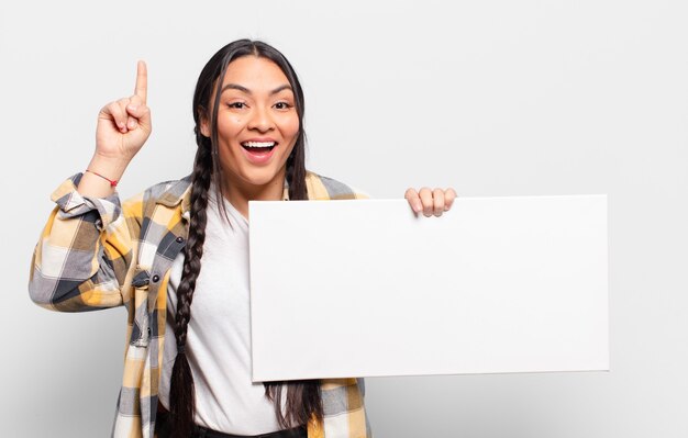 Hispanic woman feeling like a happy and excited genius after realizing an idea, cheerfully raising finger, eureka!