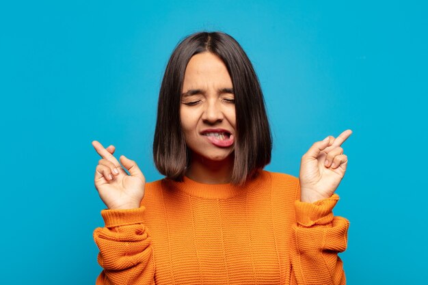 Hispanic woman feeling nervous and hopeful, crossing fingers, praying and hoping for good luck